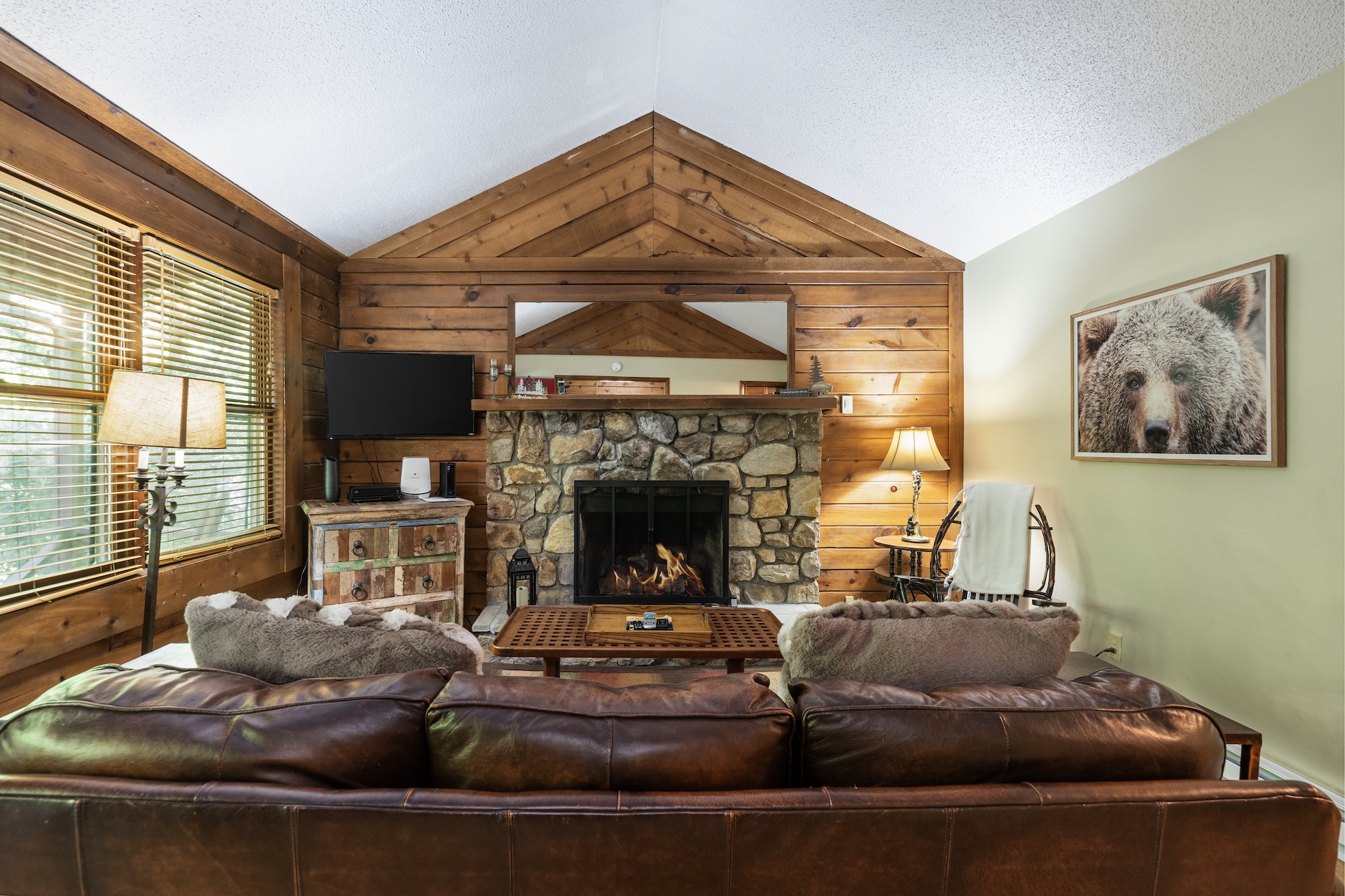 Cabin living room with stone fireplace, vaulted wood ceiling, and leather sofa